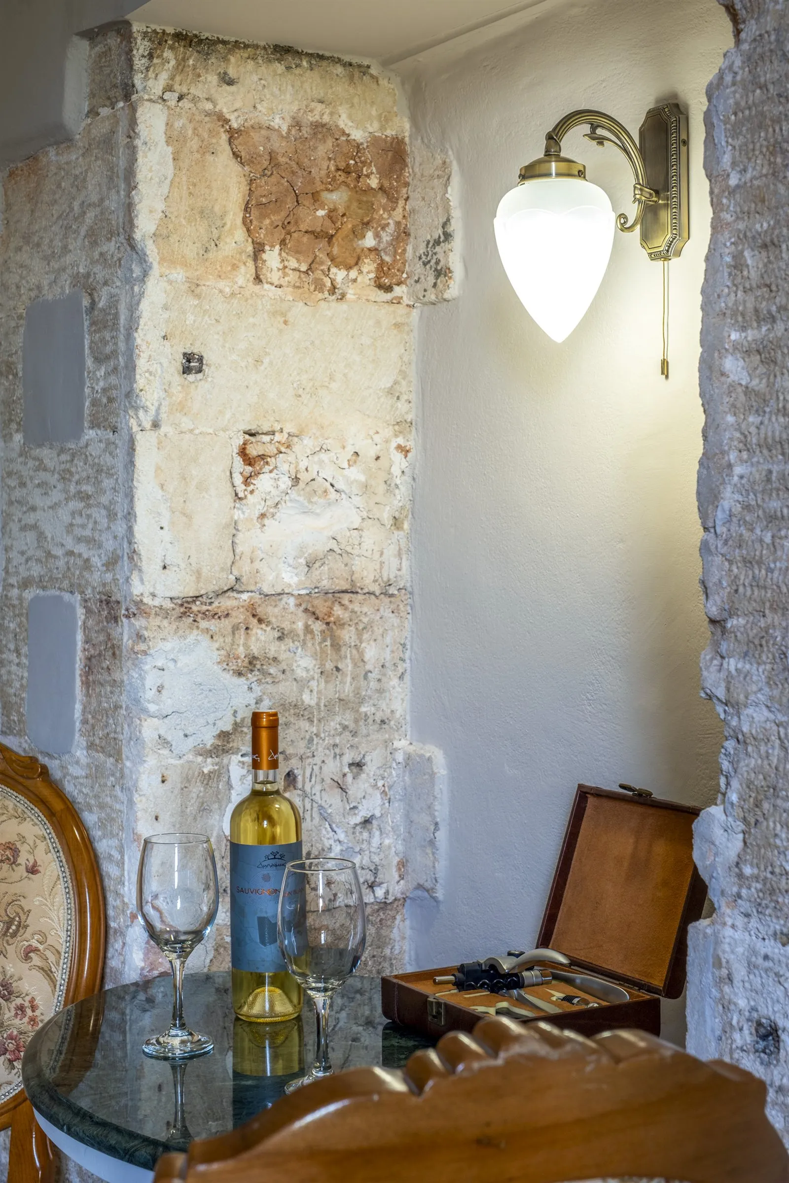 Original Venetian stone wall beside a small table with a bottle of Cretan wine