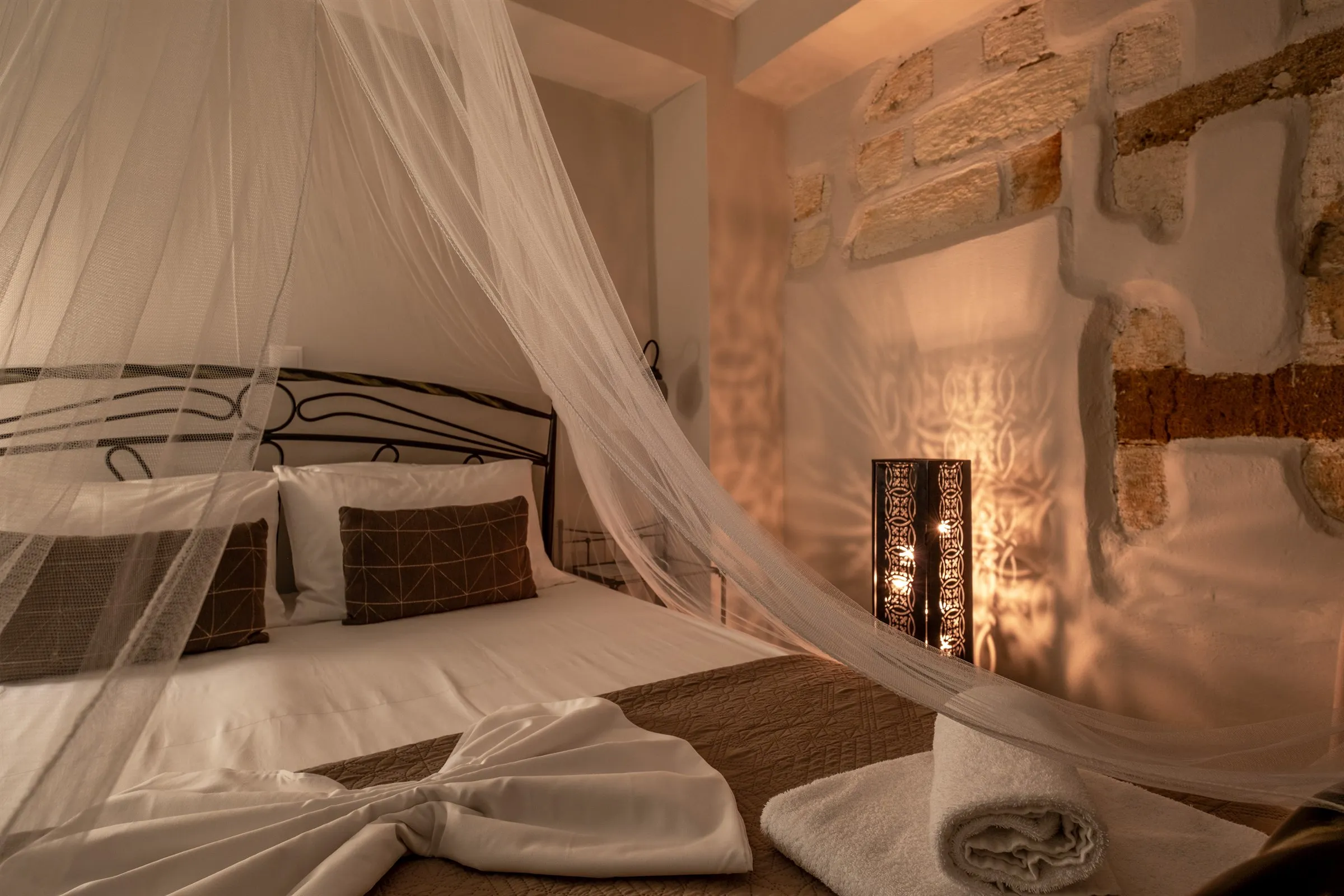 The Matilda room in the evening, a canopy bed beside exposed Venetian stonework lit by a lantern