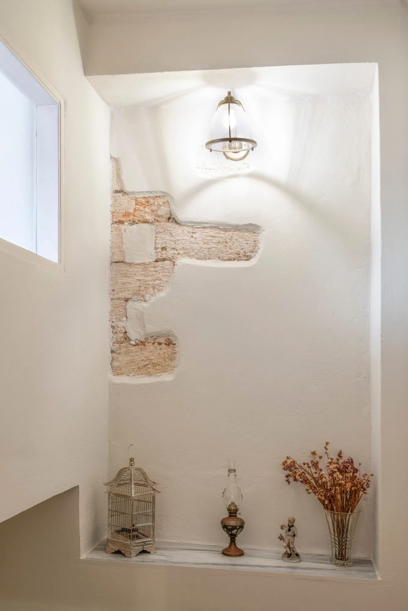 Whitewashed stairwell niche with exposed Venetian stonework, an old oil lamp and dried flowers
