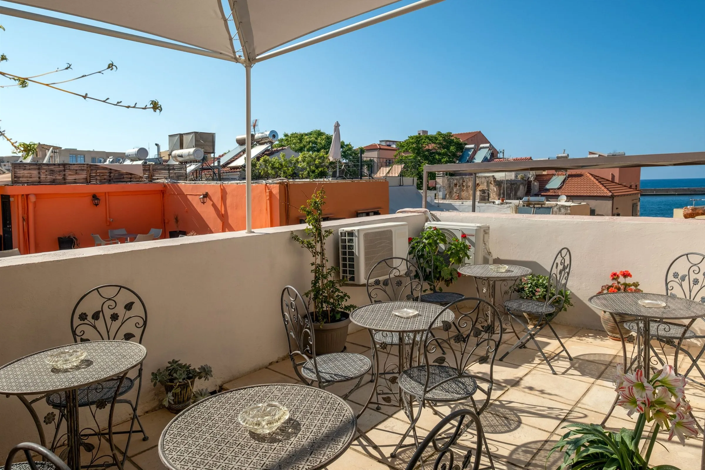 Bistro tables and plants on the roof garden, with old-town rooftops and a glimpse of the sea